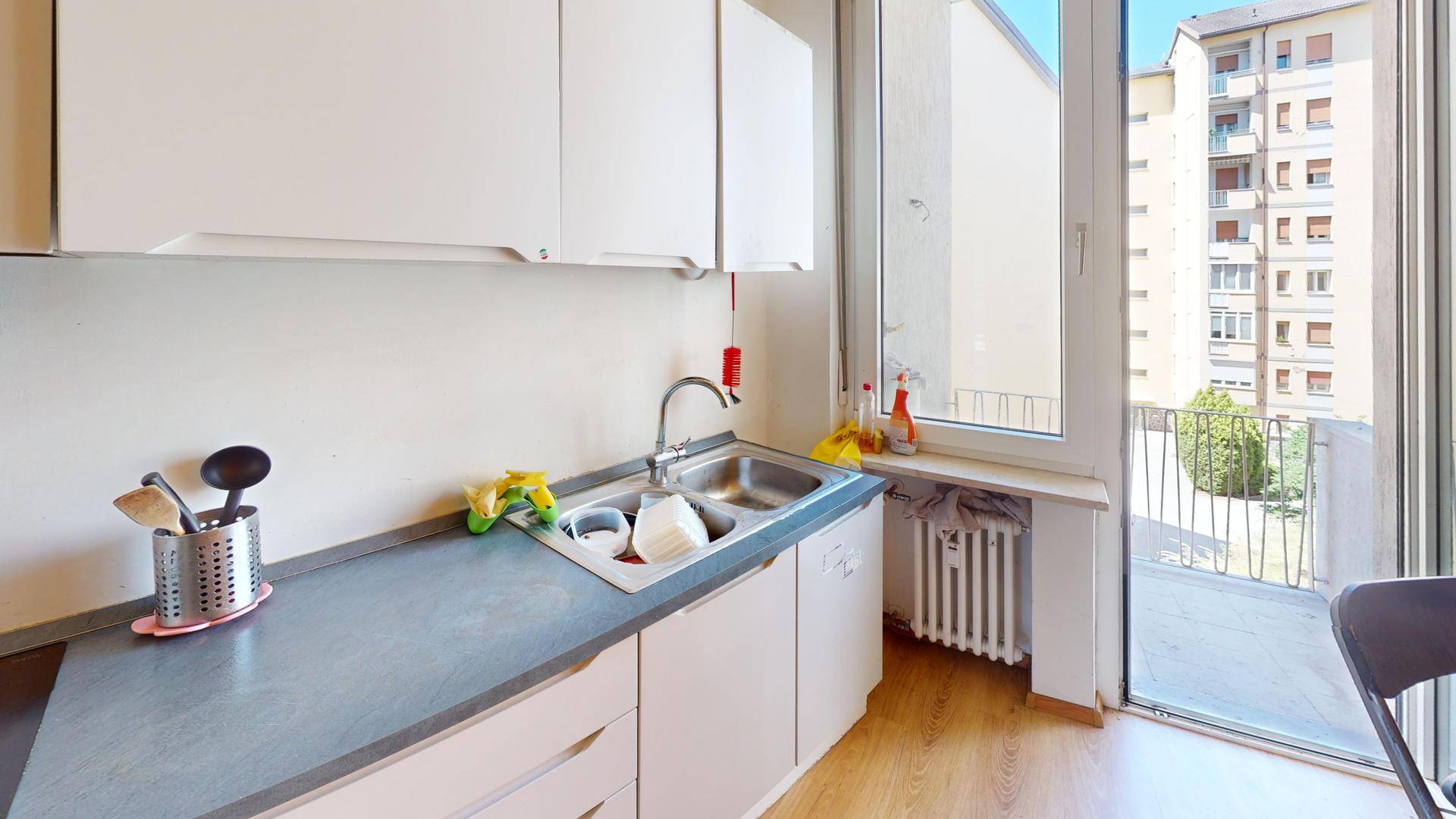 Küchenzeile mit Doppelspüle, weißen Schränken und Zugang zum Balkon.