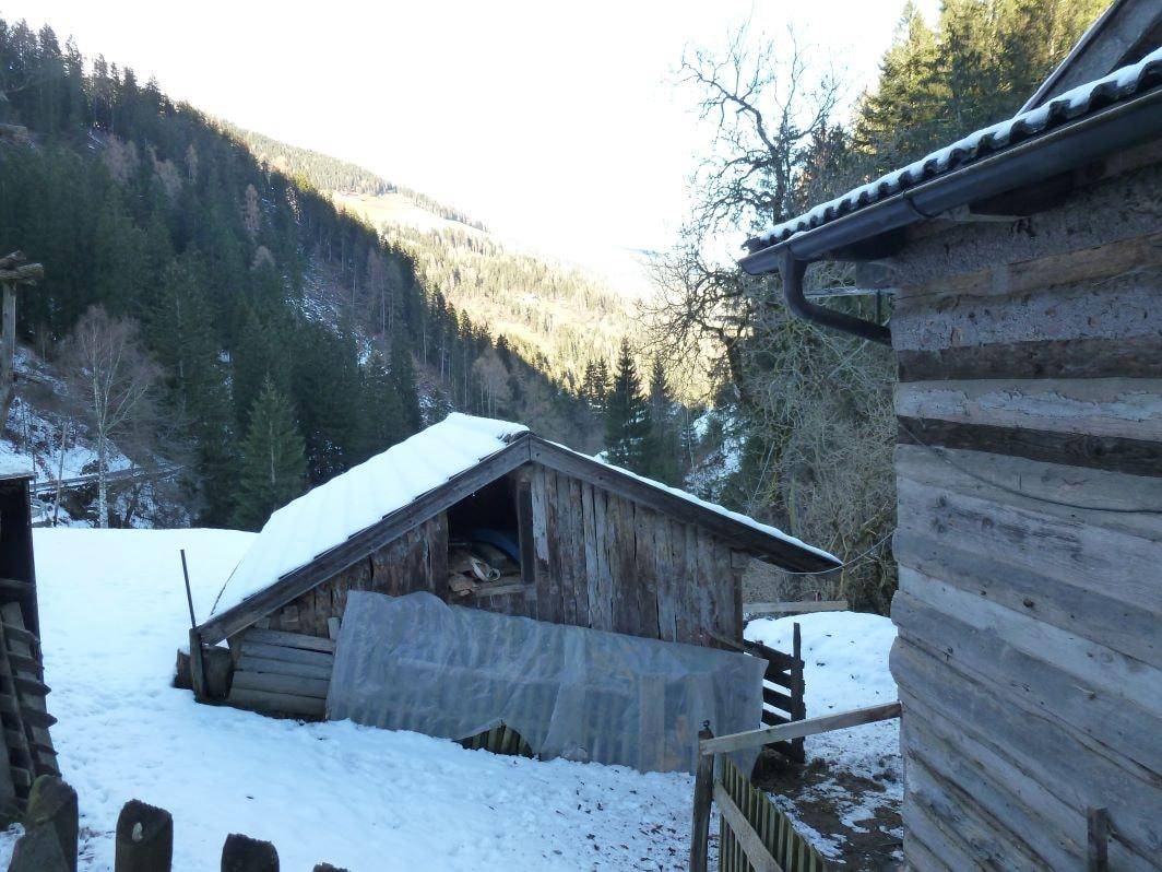 Kleiner Holzschuppen mit schneebedecktem Dach neben dem Haupthaus in winterlicher Bergumgebung.