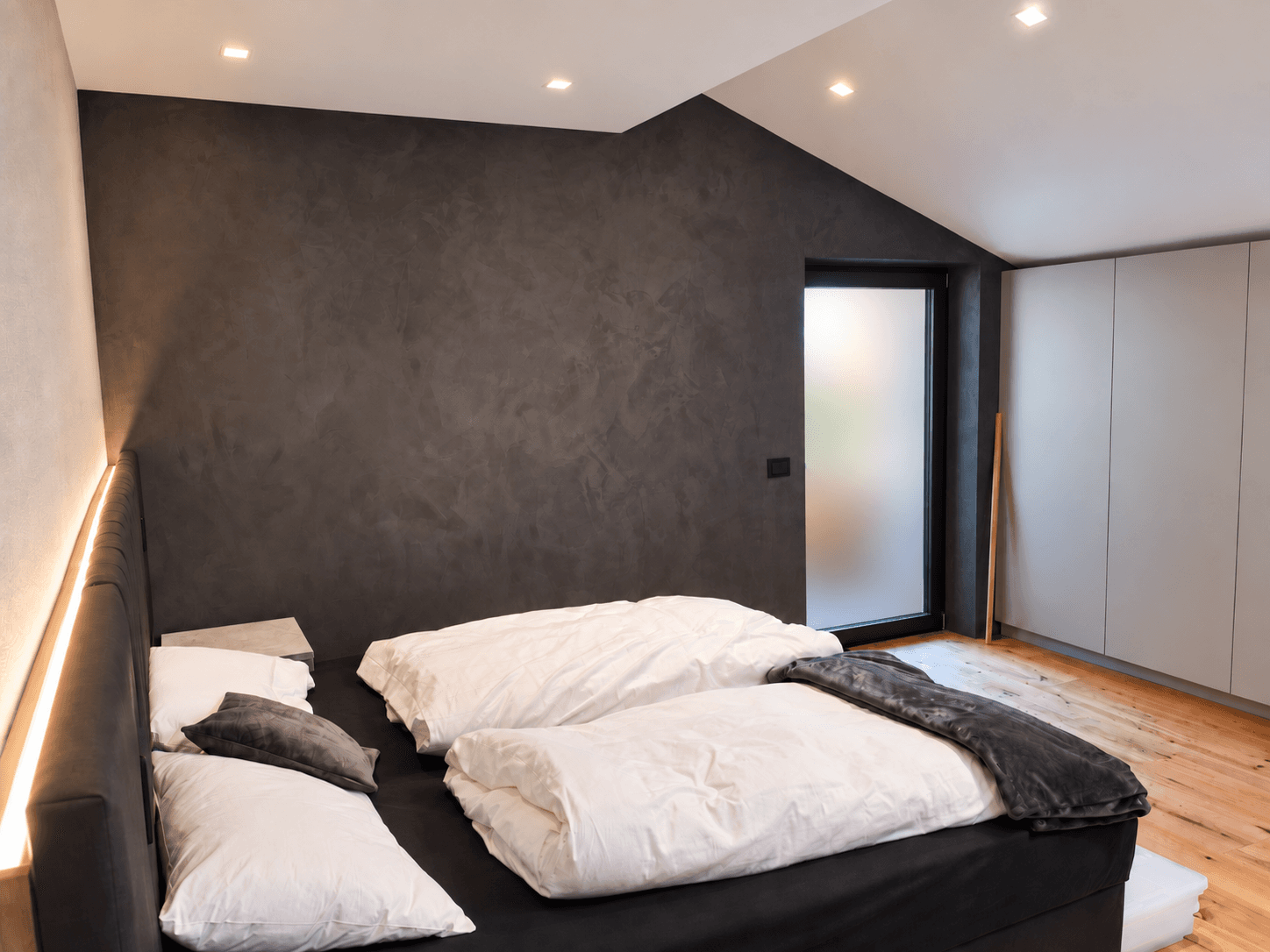 Schlafzimmer mit großem Bett, dunkler Akzentwand und Zugang zu einem Außenbereich.