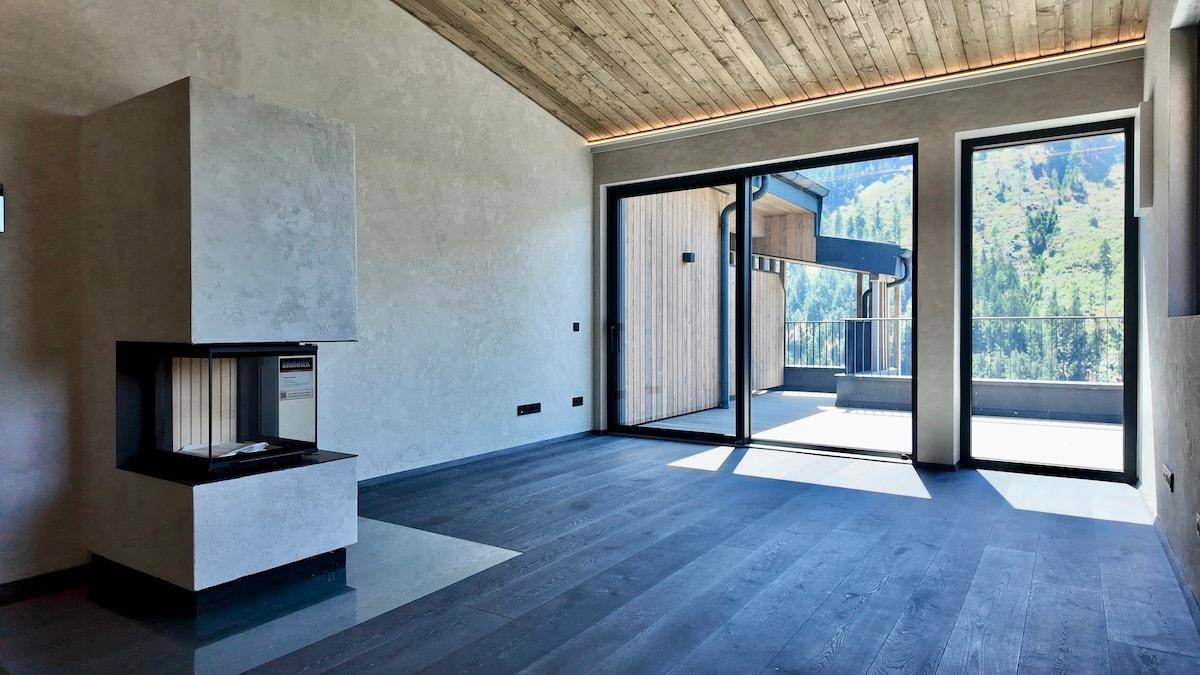 Helles Wohnzimmer mit dunklem Holzboden, modernem Kamin und Zugang zu einer Terrasse mit Bergblick.