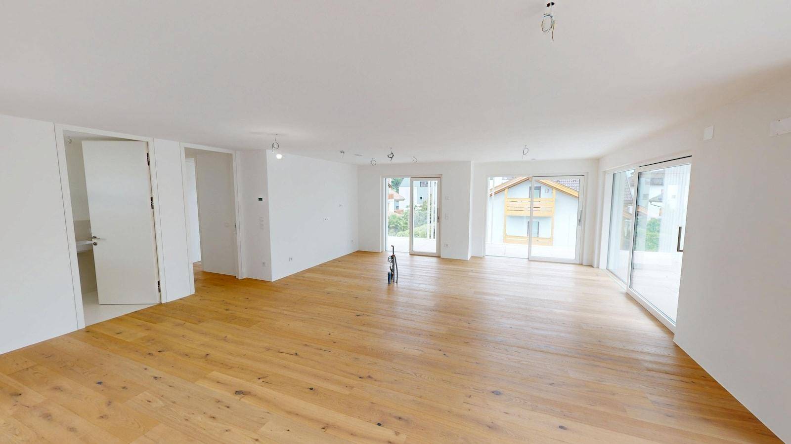 Heller, offener Wohnbereich mit hochwertigem Parkettboden und Blick ins Grüne durch große Fenster.