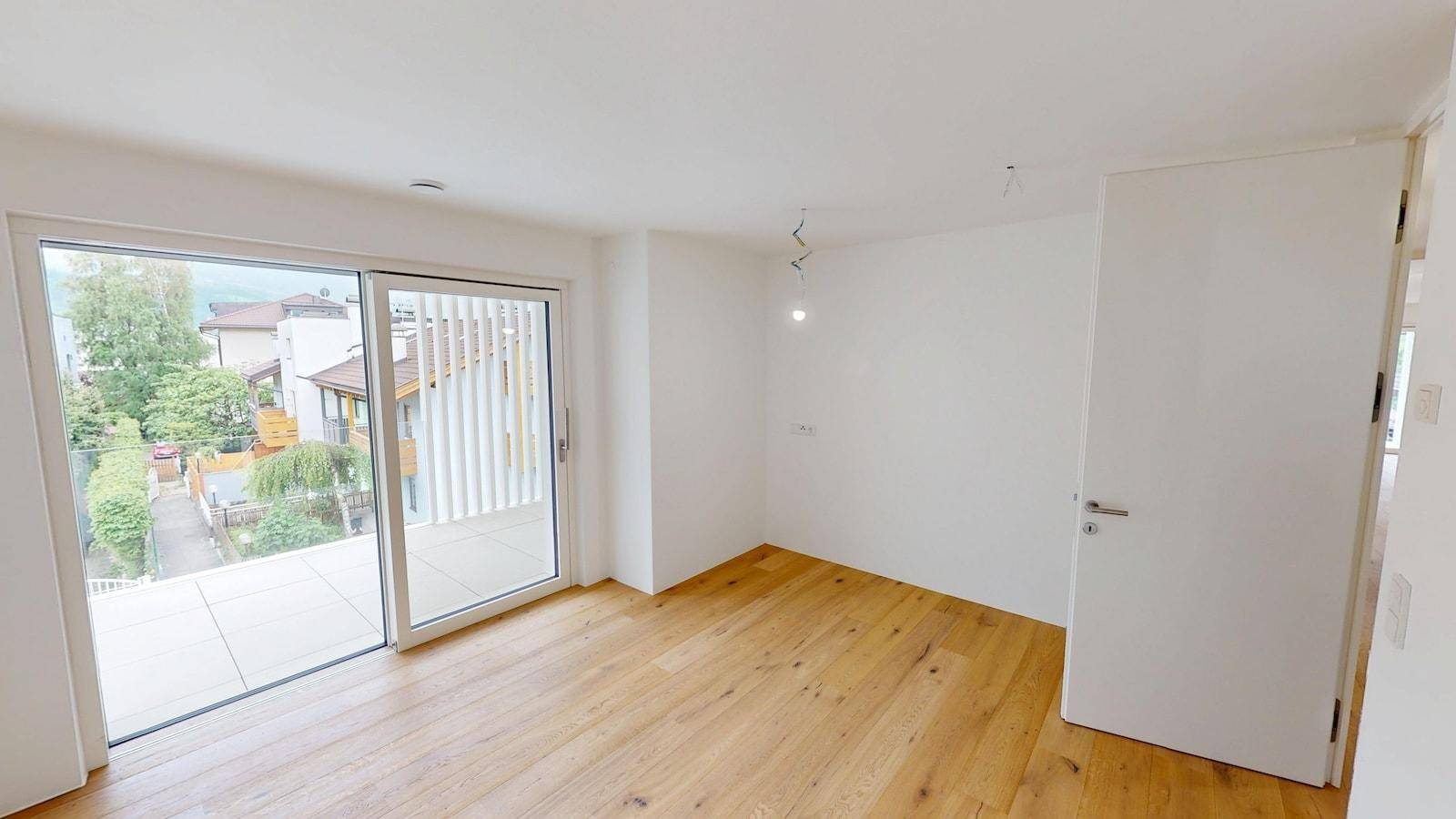 Helles Schlafzimmer mit Parkettboden und großem Schiebetürzugang zu einem Balkon oder einer Terrasse.