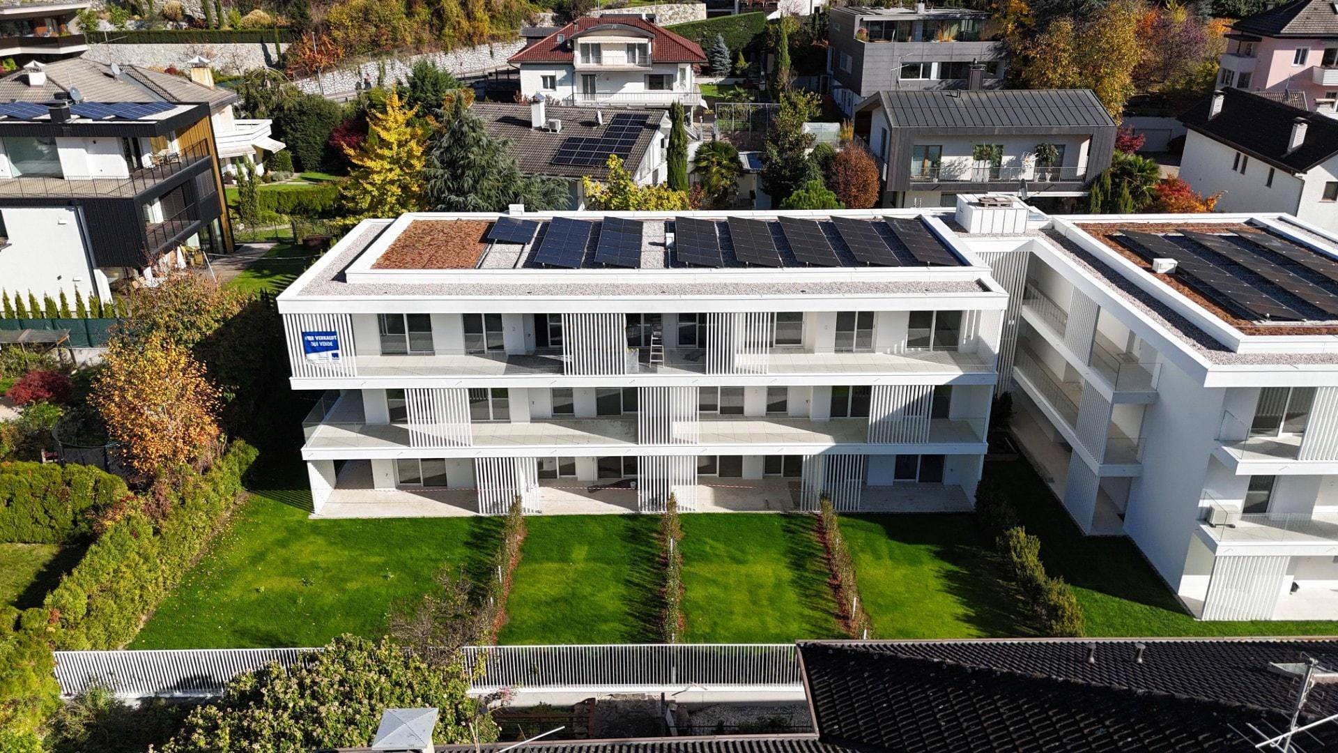 Vogelperspektive auf ein modernes Wohngebäude mit Photovoltaik auf dem Dach und gepflegten Gärten.