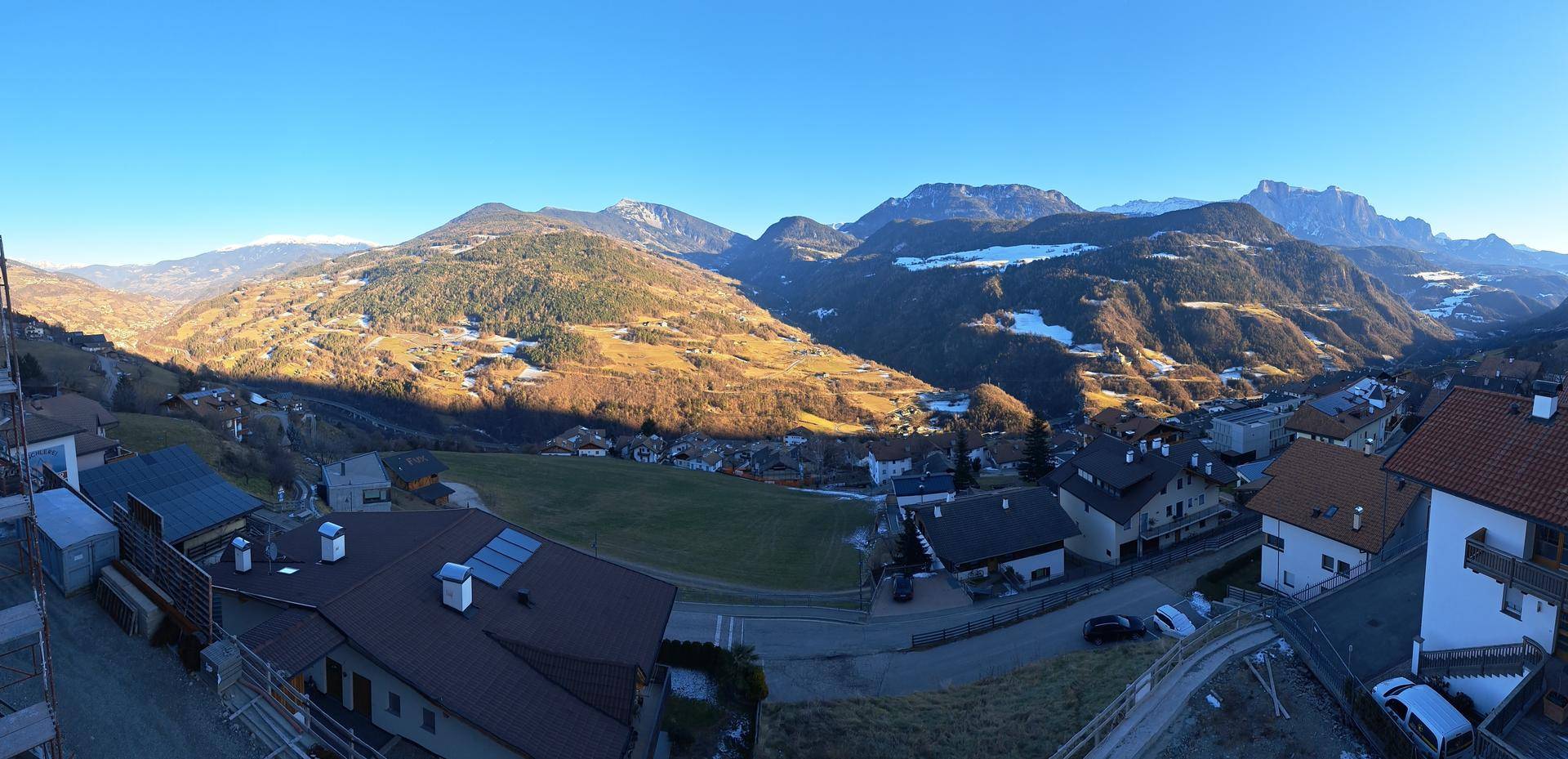 Weitläufiger Panoramablick über ein sonniges Tal mit vielen Häusern und schneebedeckten Bergen im Hintergrund.