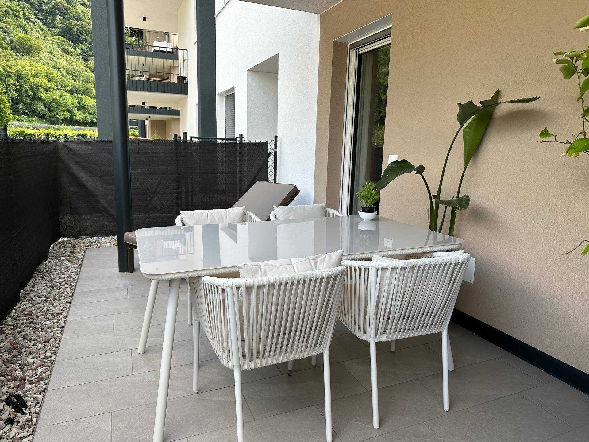 Moderne Terrasse mit Esstisch und Stühlen, umgeben von Grün.