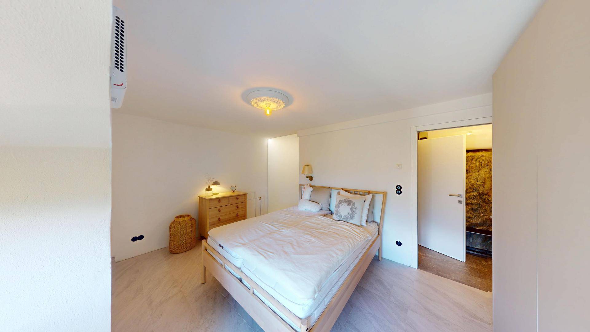 Gemütliches Schlafzimmer mit Holzbett und offenem Zugang zu einem modernen Badezimmer.