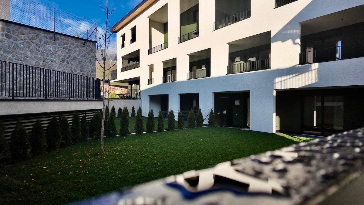 Gepflegter Rasenbereich vor einem modernen Gebäude mit Hecken und Steinmauer.