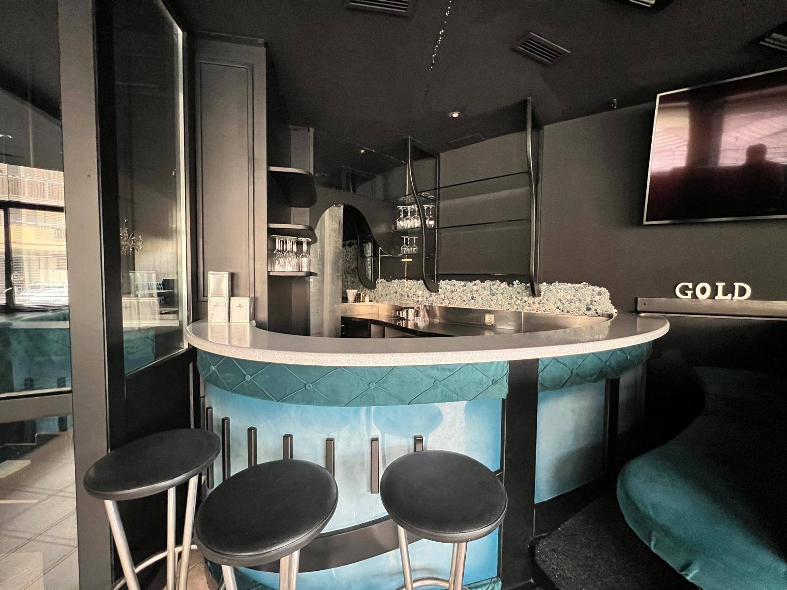 Moderne Bar mit runder Theke, Barhockern und dekorativen Elementen in dunklem Design und türkisfarbenen Akzenten.