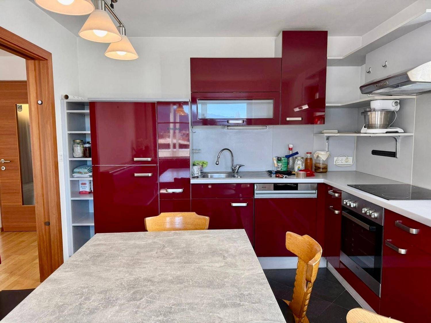 Moderne Küche in Rot mit integrierten Geräten, Essbereich und hellem Arbeitsplatten.