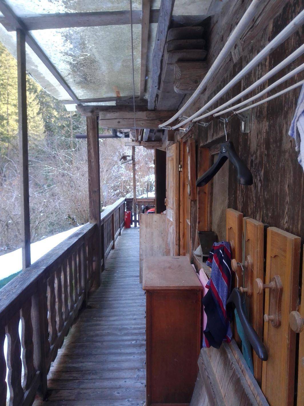 Langer, überdachter Holzbalkon mit Wäscheleine und Blick auf die umliegende Natur.