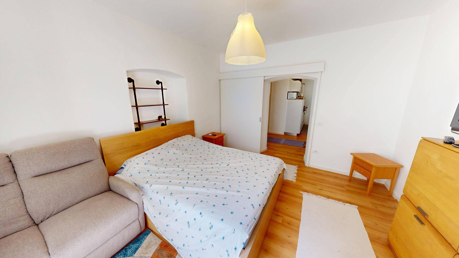 Schlafzimmer mit Holzboden, bequemer Couch und Schiebetür zum angrenzenden Wohnbereich.