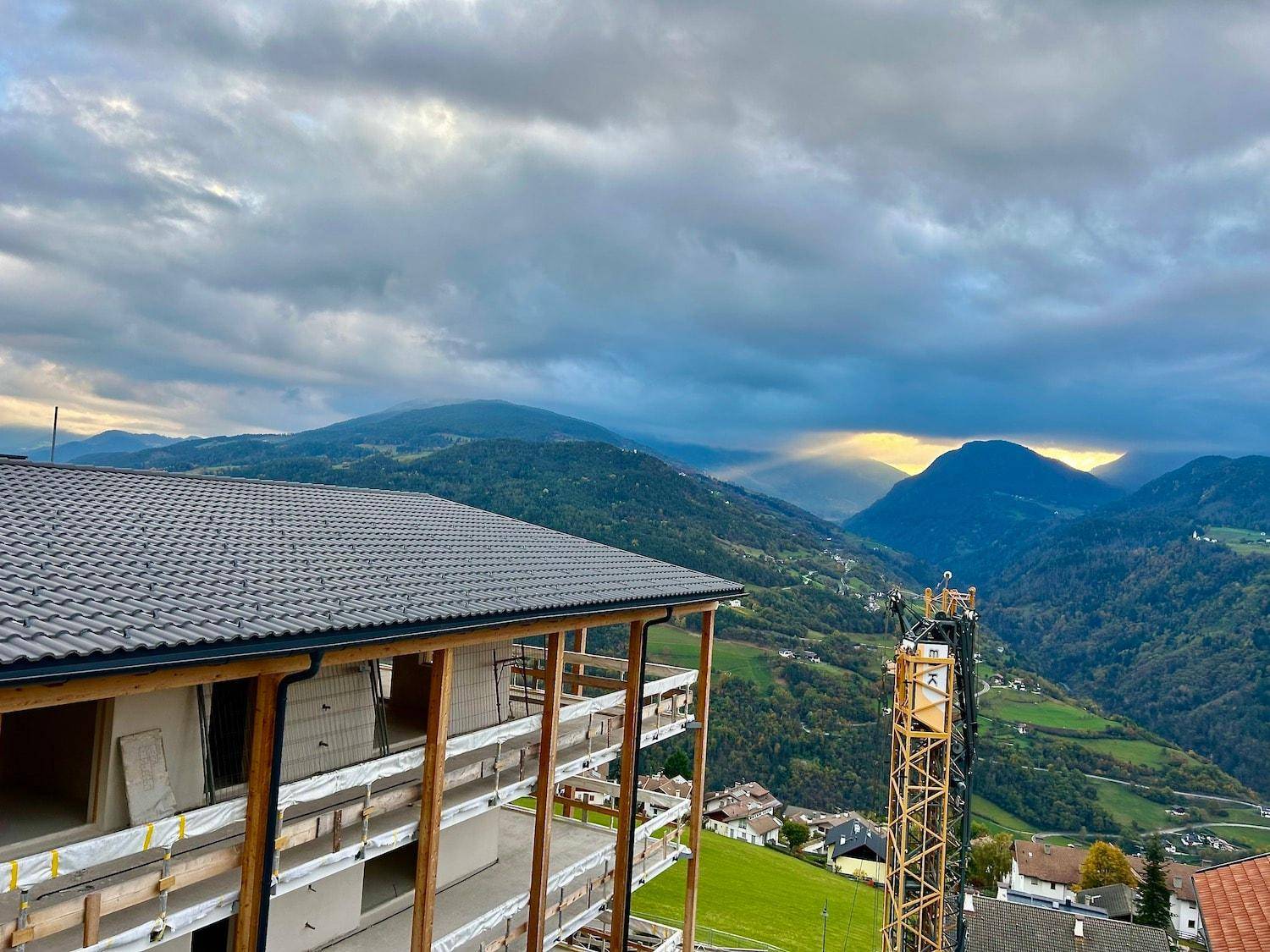 Neubau mit Blick auf eine weite Berglandschaft und ein Tal bei Sonnenuntergang.