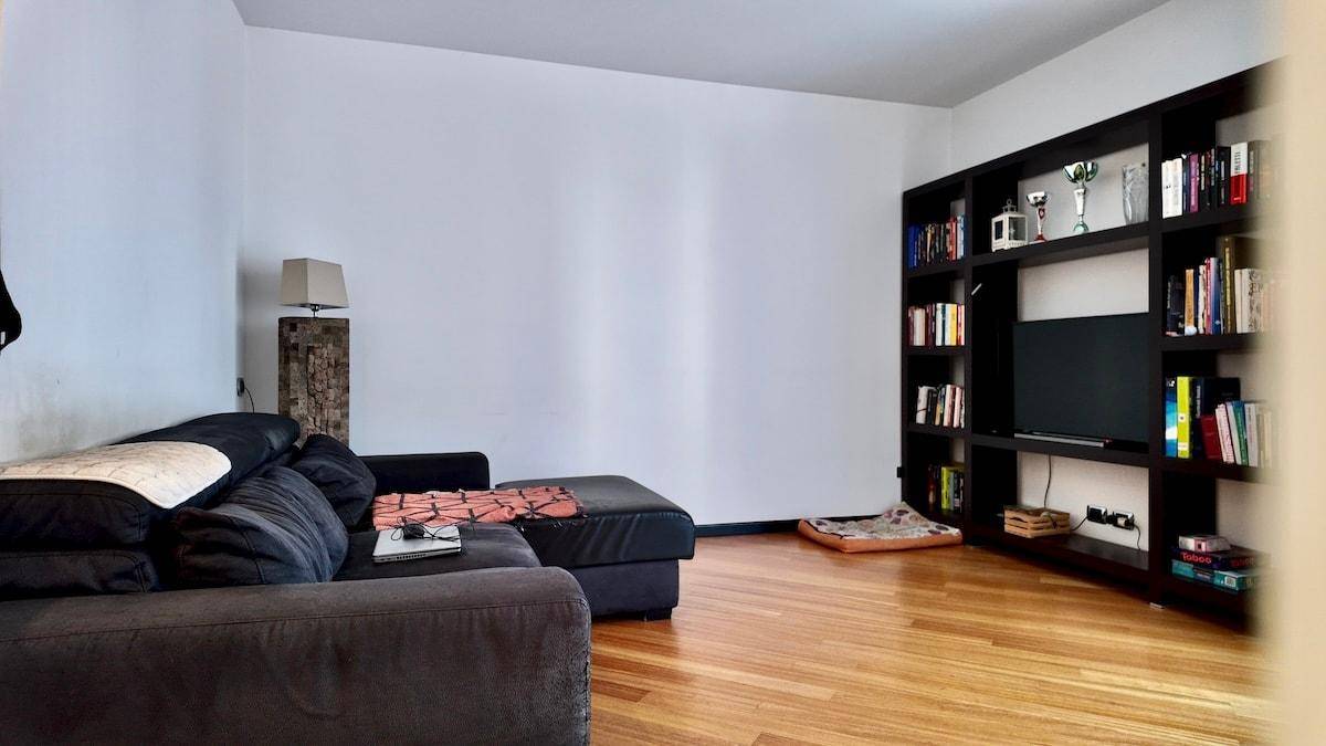 Gemütliches Wohnzimmer mit dunklem Sofa, Bücherregal und Holzboden.
