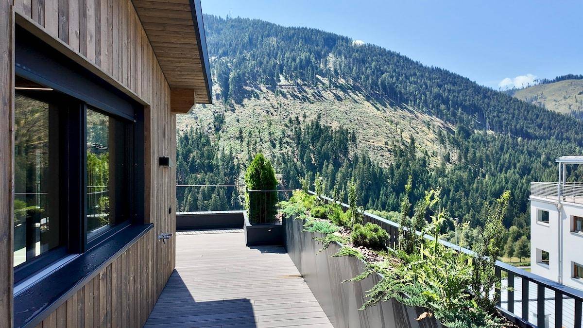 Große Terrasse mit Holzverkleidung, Pflanzen und einem weiten Blick auf die bewaldeten Berge.