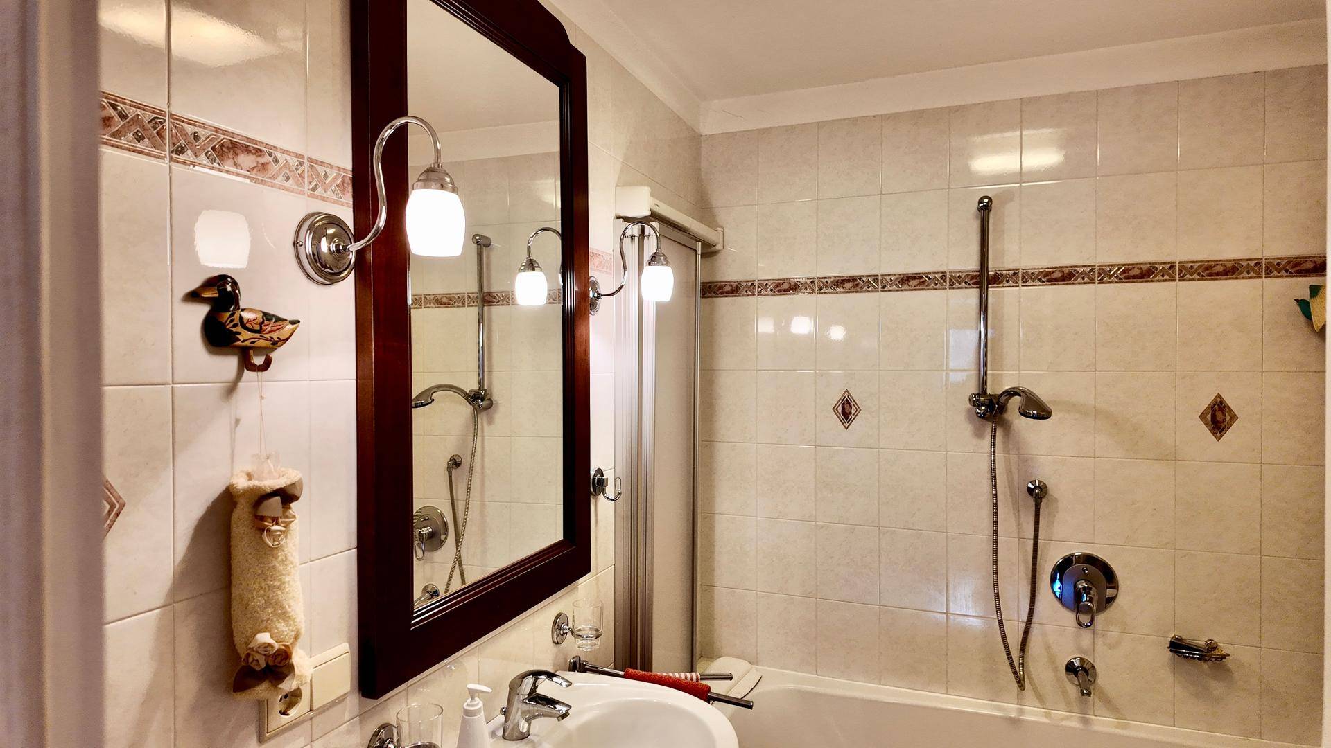Gefliestes Badezimmer mit Badewanne, Duschvorrichtung, Waschbecken und einem großen Spiegel.