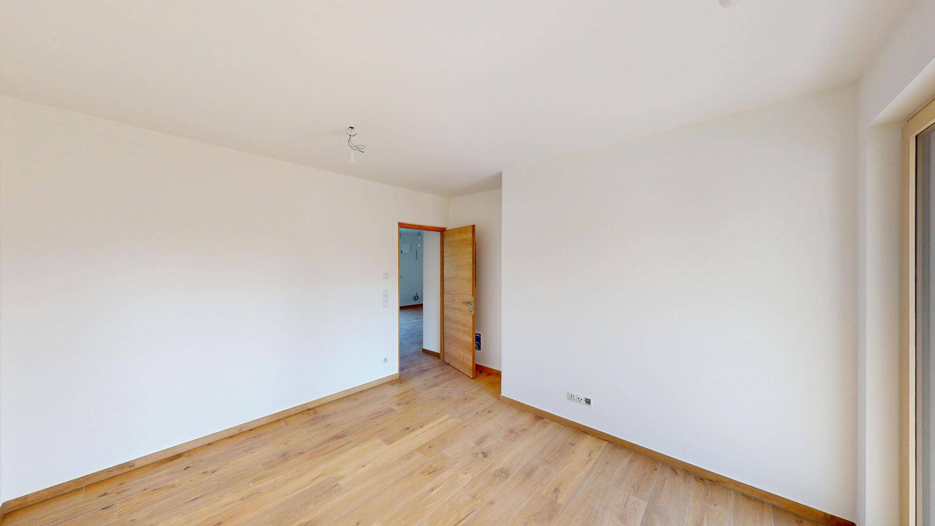 Leeres Zimmer mit hellem Holzboden und einer Holztür, bereit für die Einrichtung.