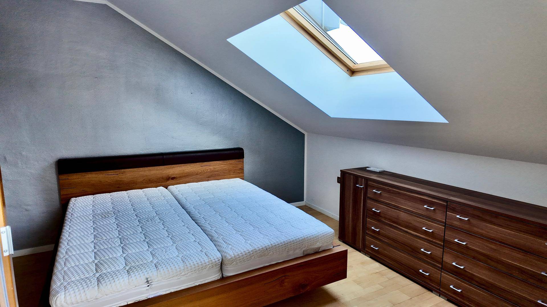 Schlafzimmer im Dachgeschoss mit Holzbett, Kommode und einem hellen Dachfenster.