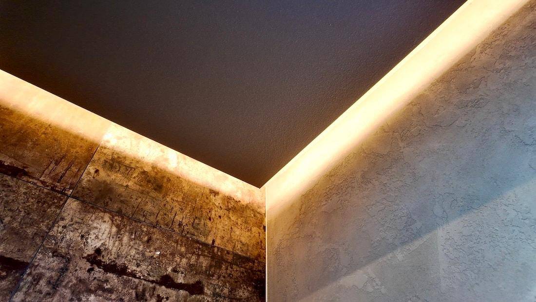 Raumdetail mit dunkler Decke, strukturierten Wänden und indirekter LED-Beleuchtung.