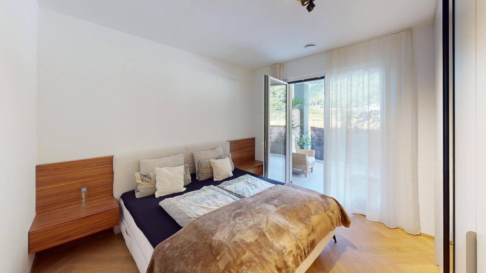 Helles Schlafzimmer mit Doppelbett und Zugang zu einem Balkon oder einer Terrasse.