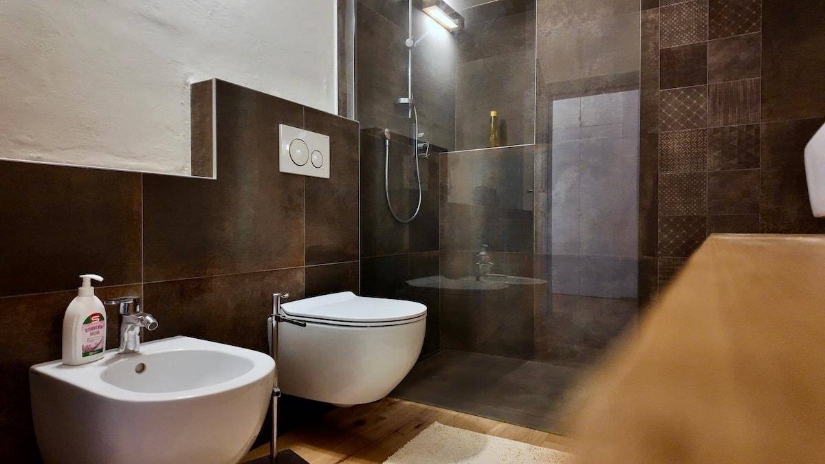 Badezimmer mit moderner Dusche, wandhängendem WC und Bidet in dunklen Fliesen.