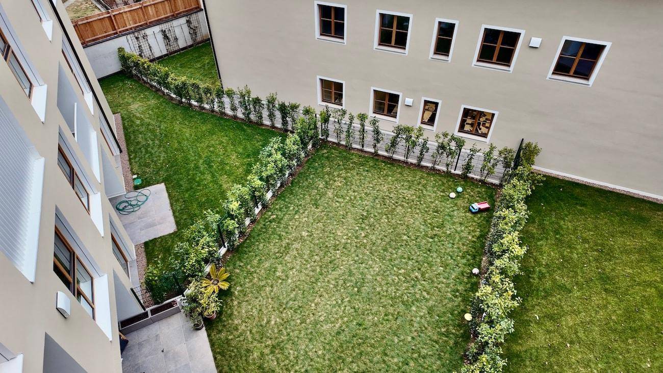 Gepflegte Gartenanlage mit Rasenflächen und Hecken, umgeben von modernen Wohngebäuden.