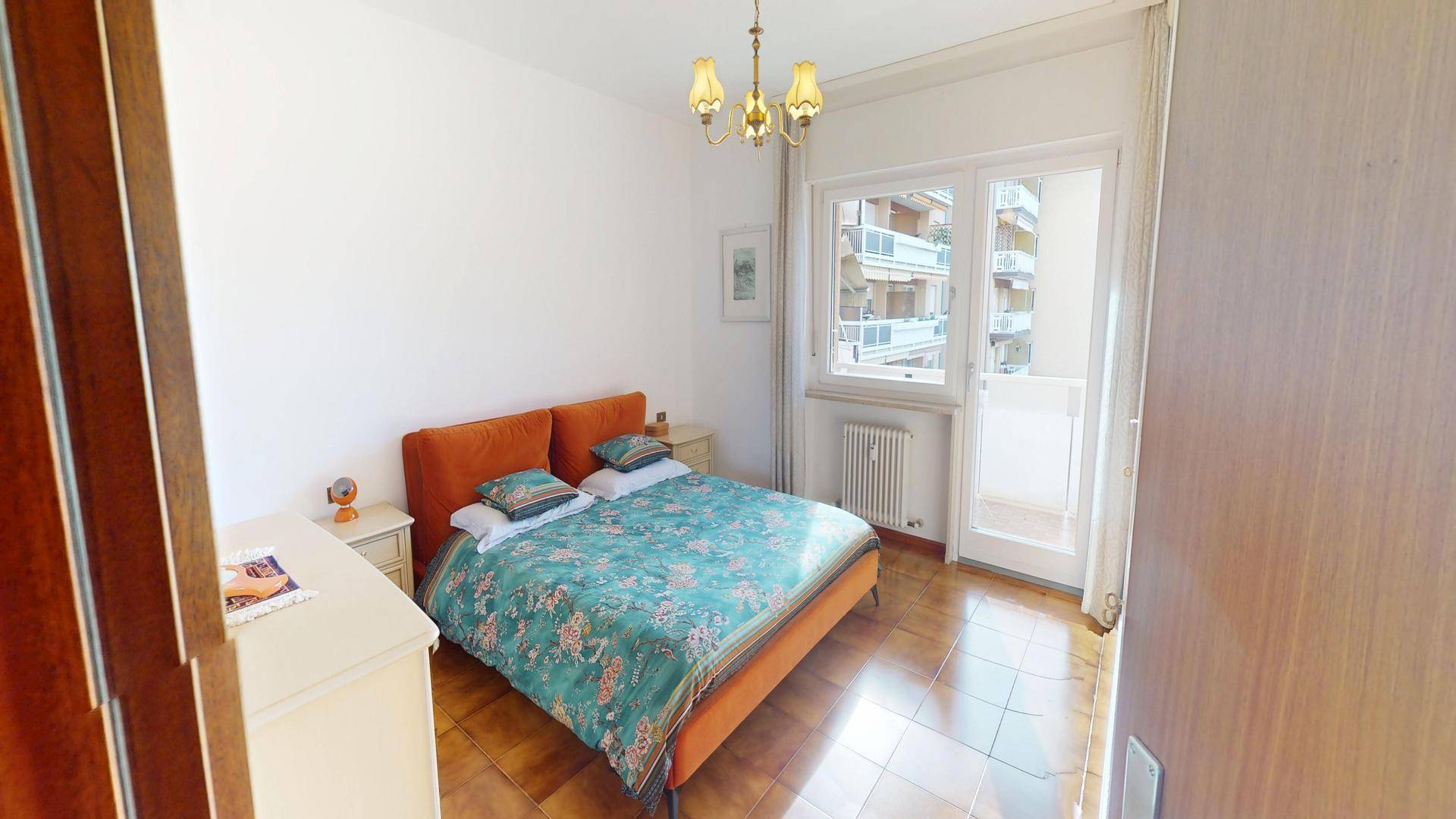 Helles Schlafzimmer mit Doppelbett, Fliesenboden und Balkonzugang.
