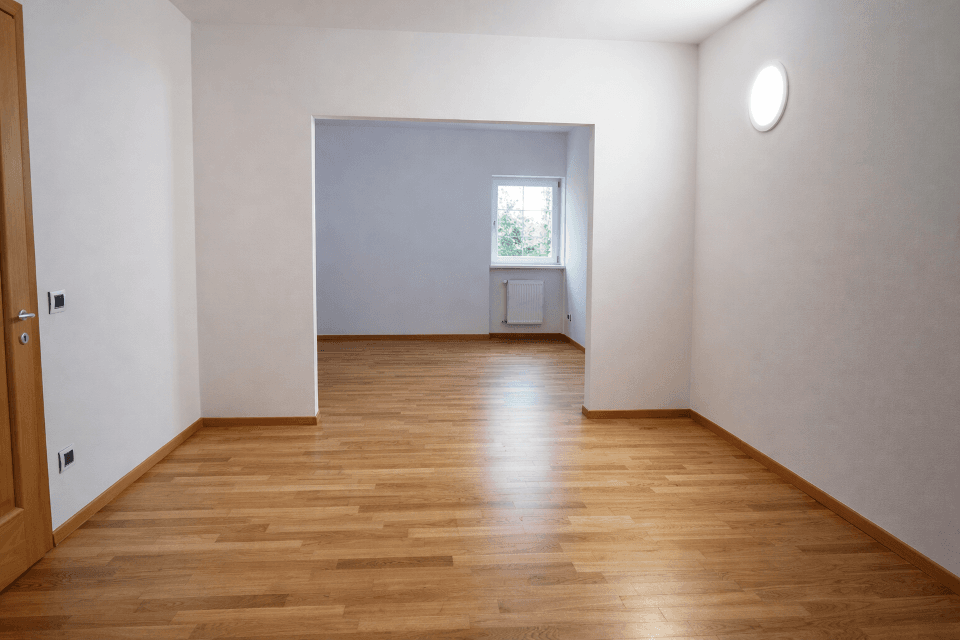Leerer Raum mit Holzboden, Fenster und offenem Durchgang zu einem weiteren Bereich.