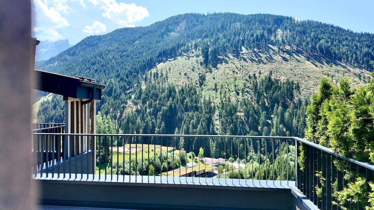 Panoramablick von der Terrasse auf die majestätischen Berge und das grüne Tal mit vereinzelten Häusern.
