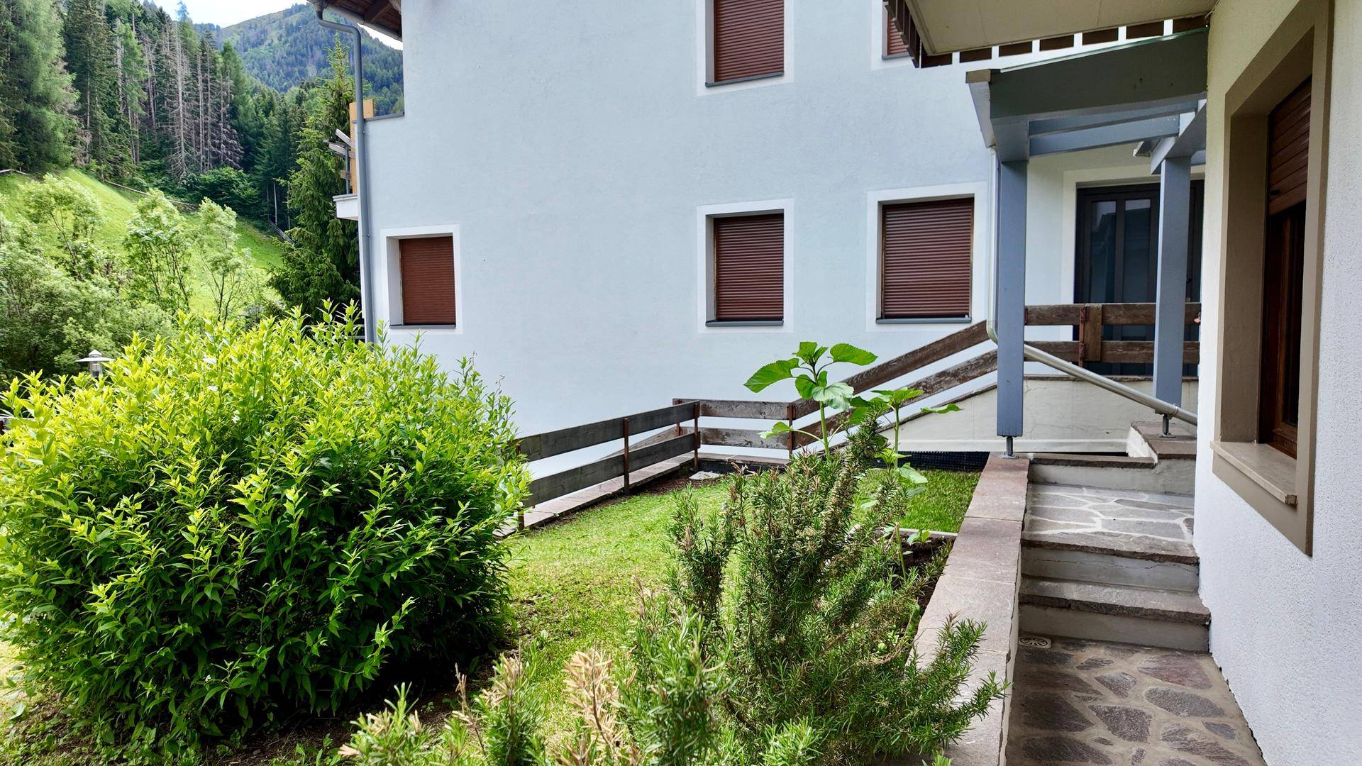 Außenansicht des Gebäudes mit weißer Fassade, braunen Fensterläden und einem kleinen Vorgarten.