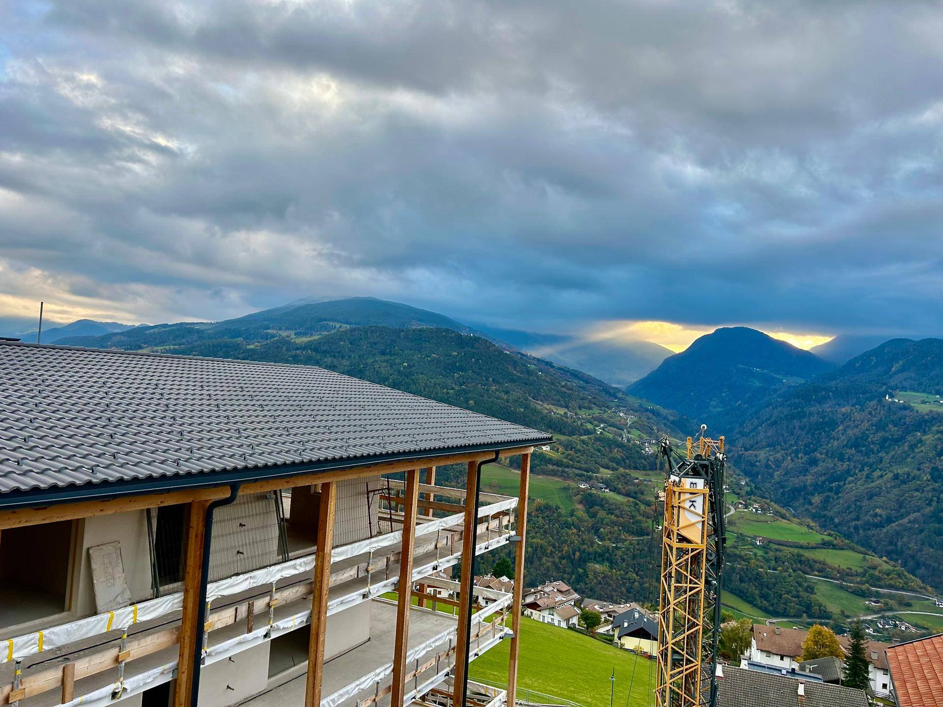 Blick auf den Neubau in Bauphase mit beeindruckendem Bergpanorama und Sonnenstrahlen am Horizont.