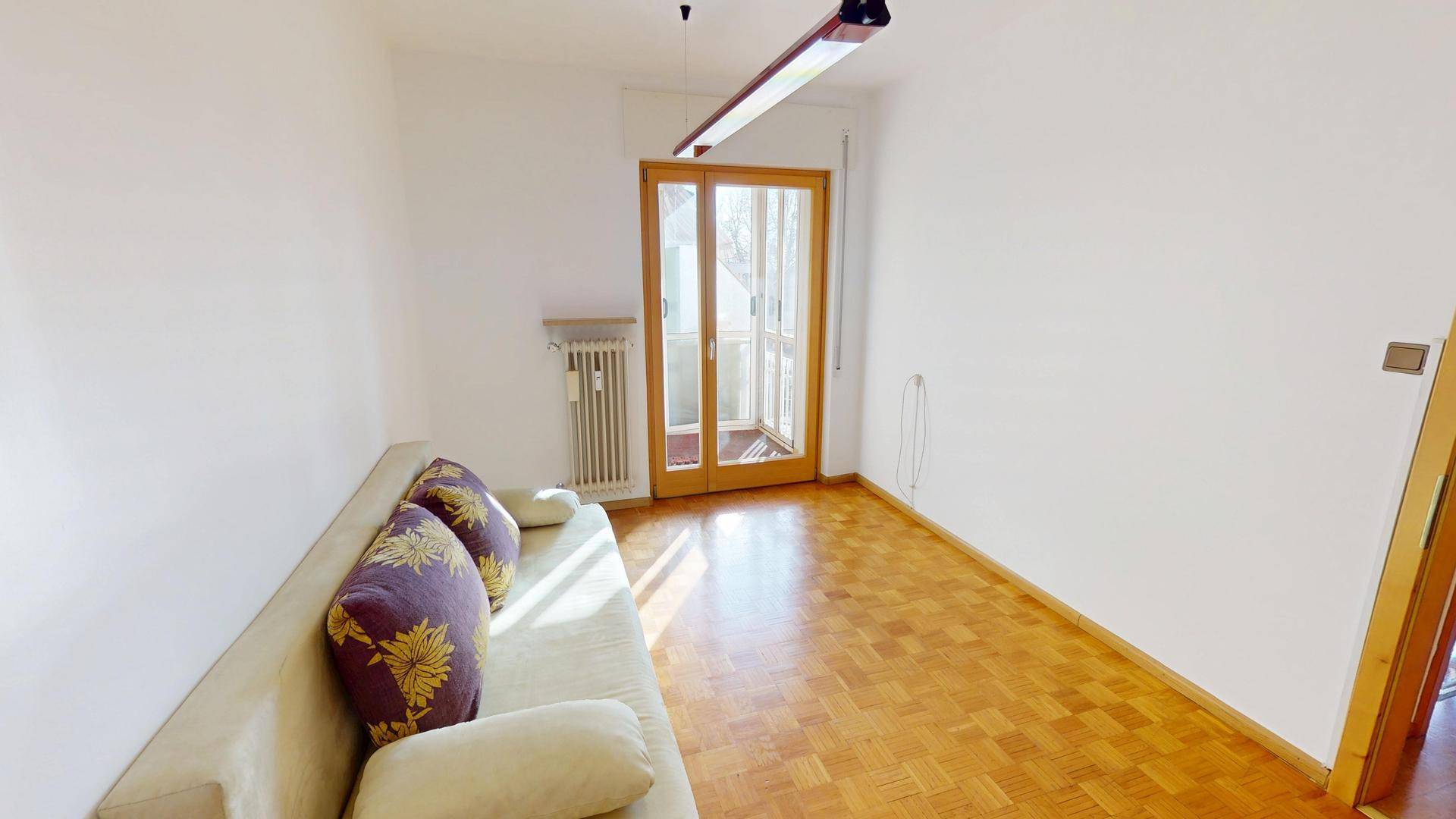 Wohnzimmer mit Sofa, Parkettboden und Zugang zu einem französischen Balkon.