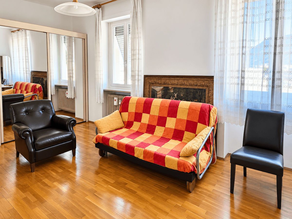 Geräumiges Schlafzimmer mit Schlafsofa, Ledersessel und einem großen Spiegelschrank, der viel Licht reflektiert.
