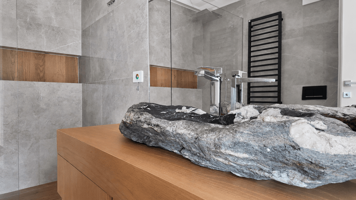 Modernes Badezimmer mit grauen Fliesen, einzigartigem Steinwaschbecken und begehbarer Dusche.