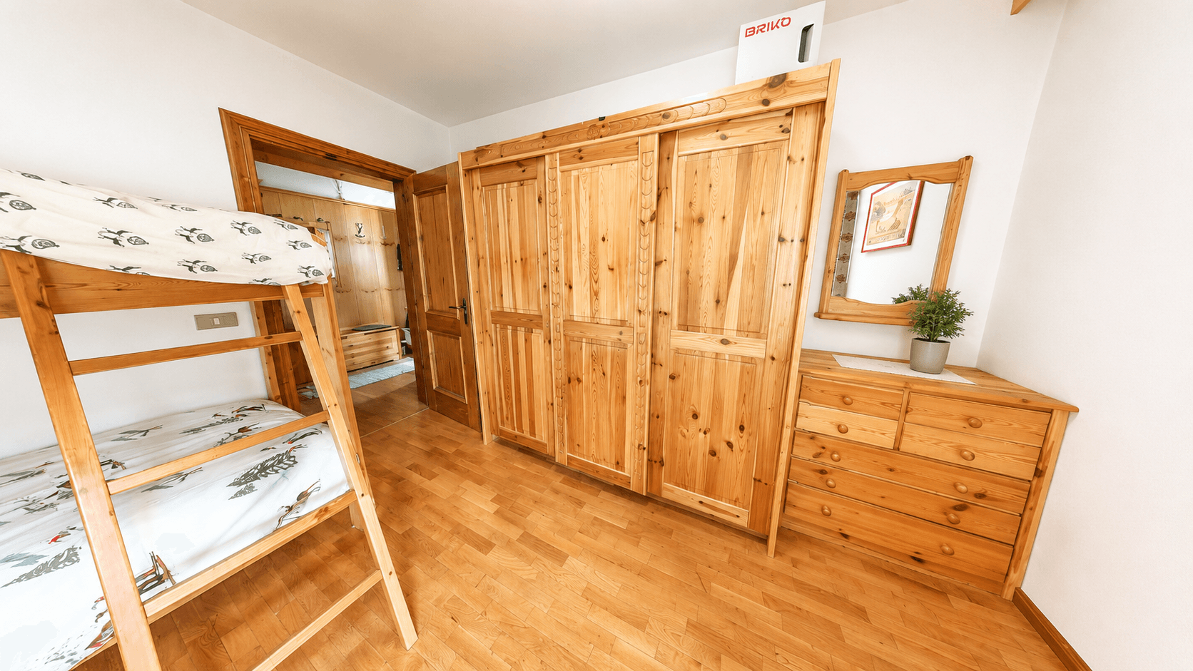 Helles Schlafzimmer mit Etagenbett, Holzschränken und Kommode mit Spiegel.