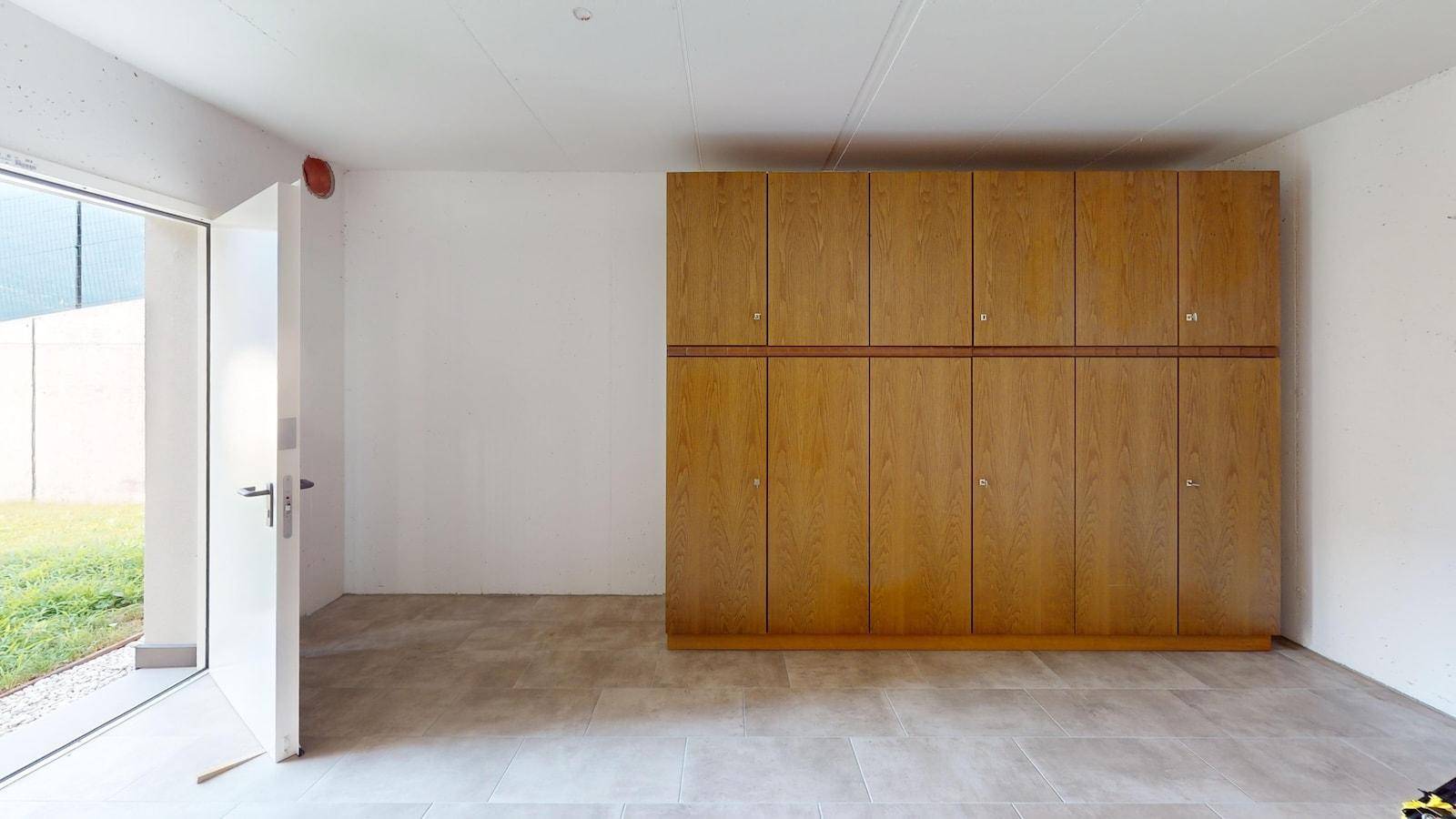Geräumiger Raum mit Fliesenboden, großem Holzschrank und direktem Zugang zum Garten.