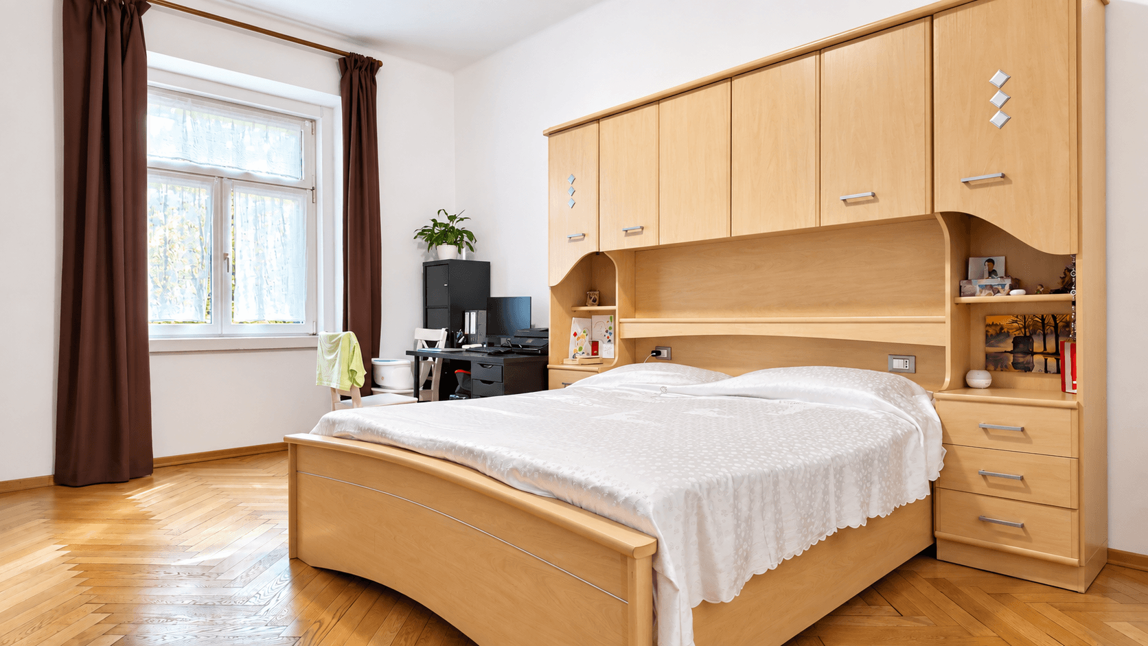 Schlafzimmer mit großem Bett, integrierten Holzschränken und Parkettboden.