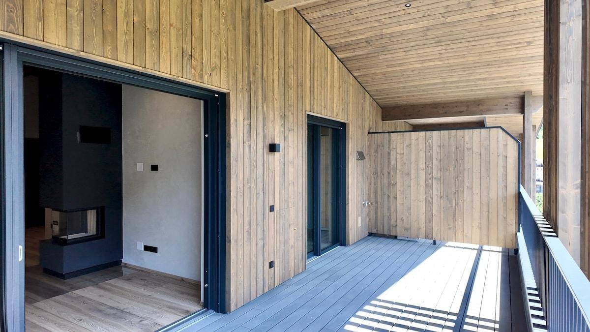 Moderner Balkon mit Holzverkleidung und Zugang zu einem Innenraum mit Kamin.