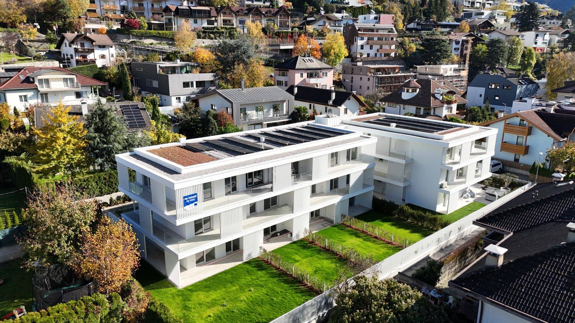 Luftaufnahme einer modernen Wohnanlage mit Solaranlagen auf dem Dach und Gärten.