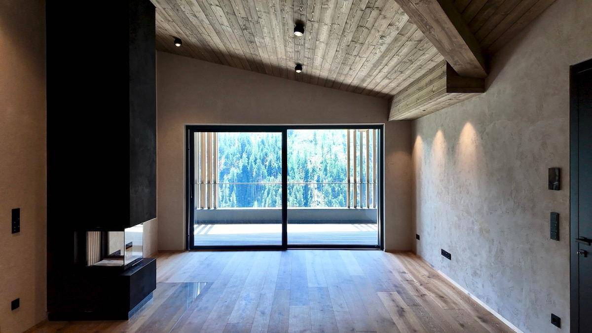 Helles Wohnzimmer mit Holzboden, modernem Kamin und großem Fenster mit Bergblick.