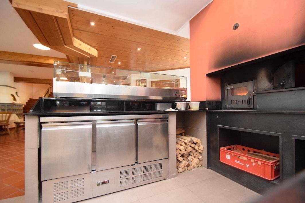 Professionelle Küche mit einem traditionellen Pizzaofen, Edelstahlgeräten und Holzvorrat.