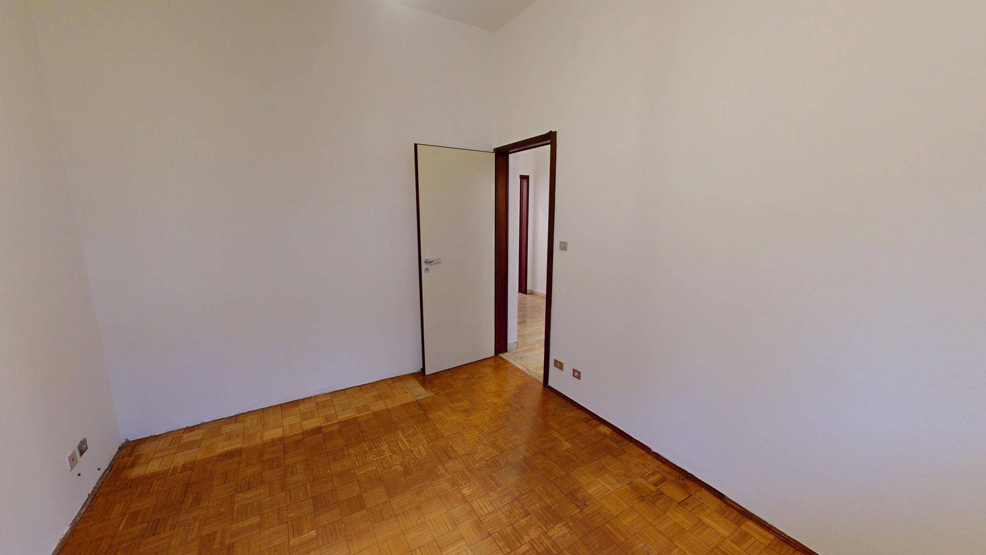 Leeres Zimmer mit Parkettboden und einer Tür, die den Zugang zu weiteren Räumen ermöglicht.