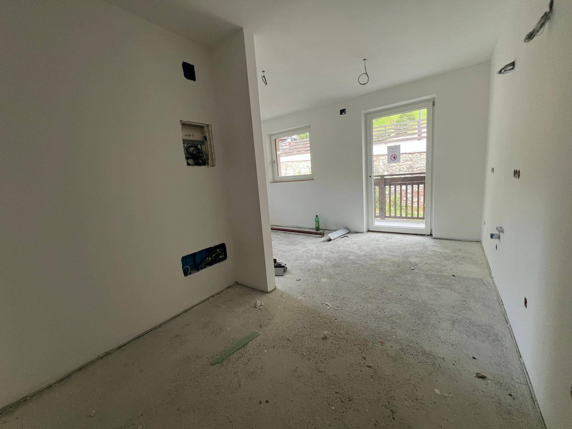 Unfertiger Innenraum mit Rohbauwänden, Betonboden und Zugang zu einem Balkon.