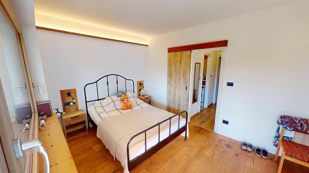 Schlafzimmer mit Holzboden, Doppelbett und Schiebetür zu einem weiteren Raum.