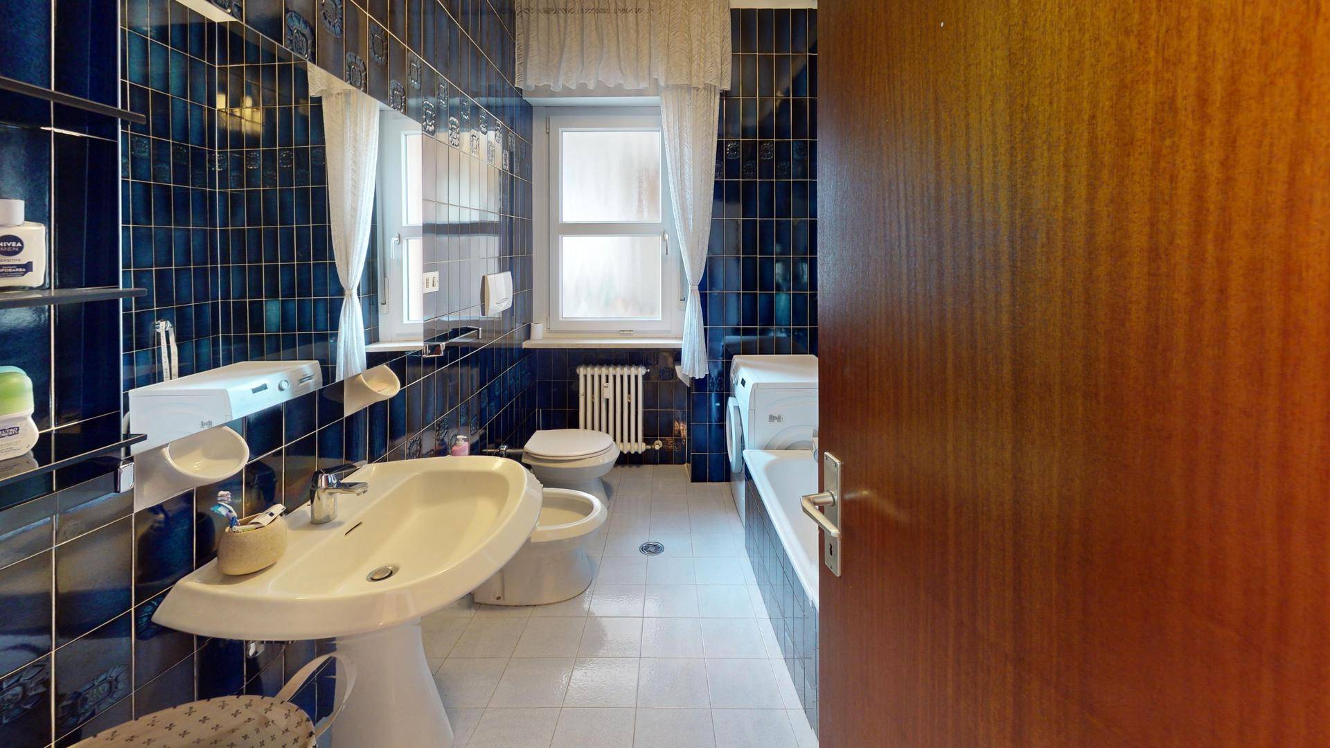 Badezimmer mit blauen Fliesen, Badewanne, WC und Fenster.