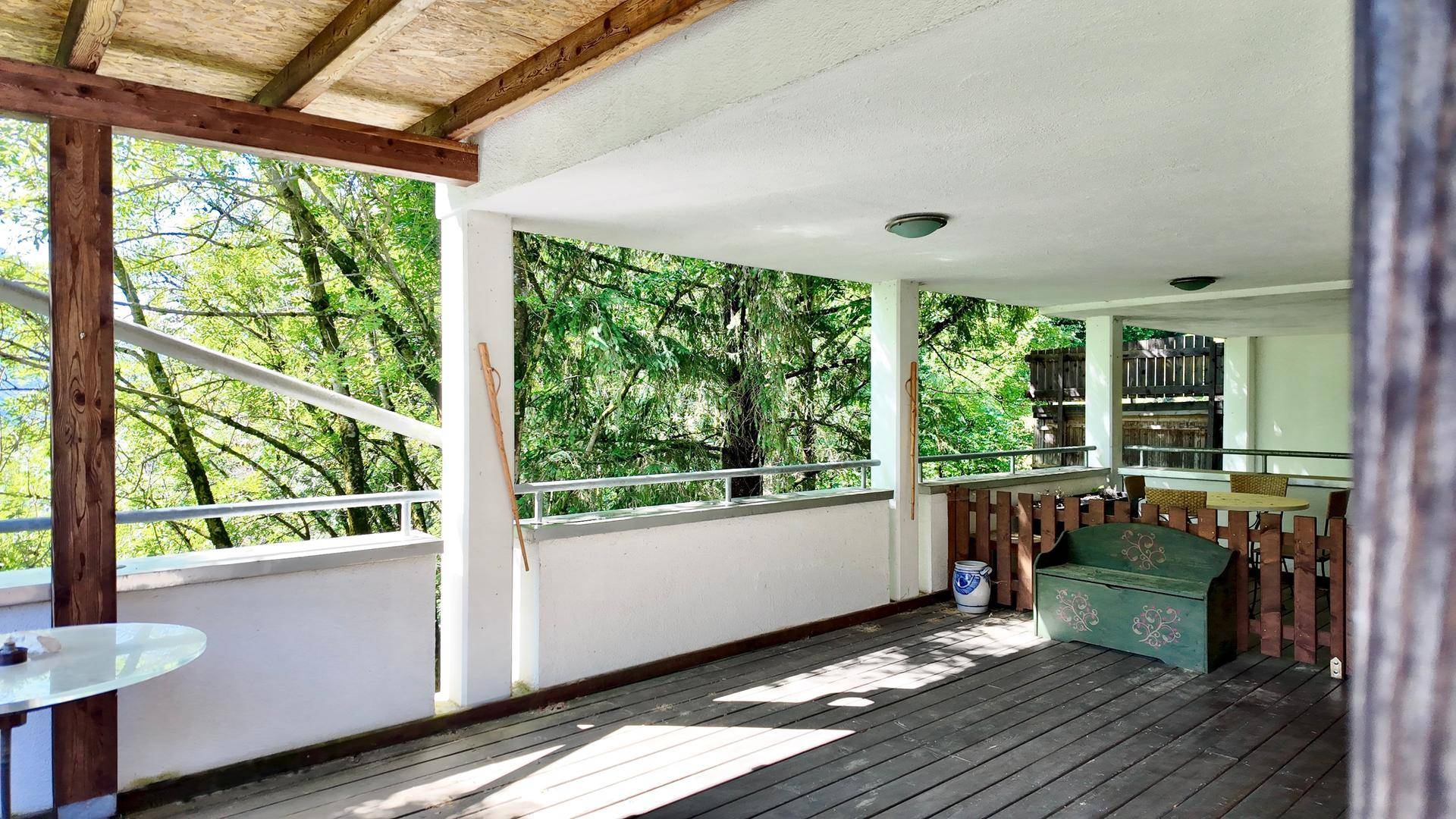 Geräumiger überdachter Balkon mit Holzboden und einer rustikalen Holzbank, ideal zum Entspannen.