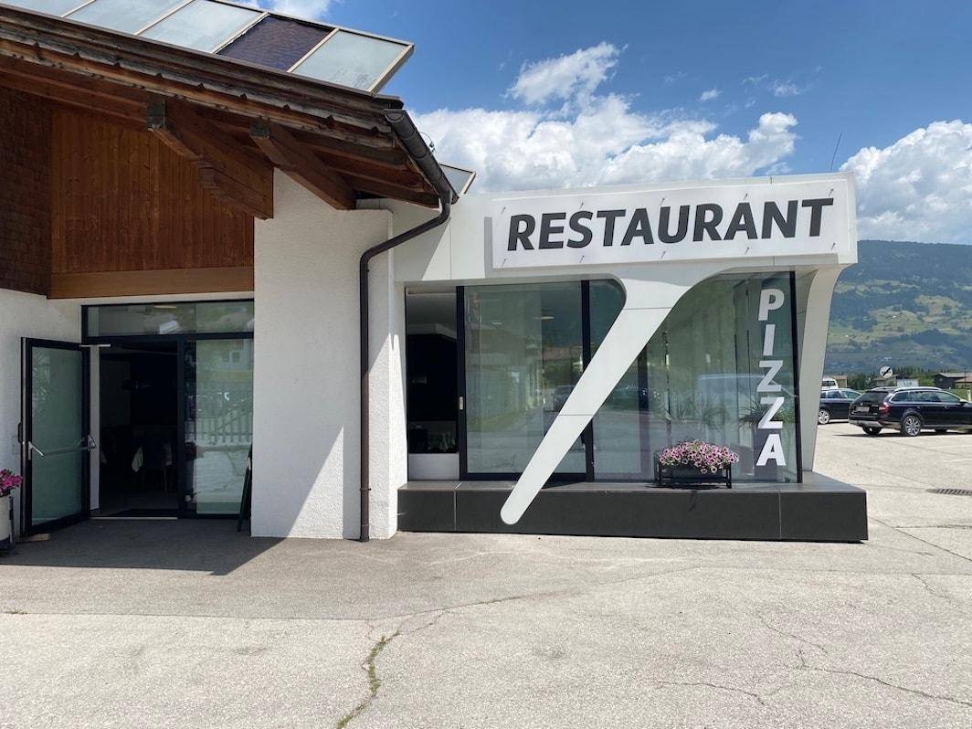 Moderne Restaurantfassade mit großen Glasflächen, auffälliger Beschilderung und Parkmöglichkeiten.