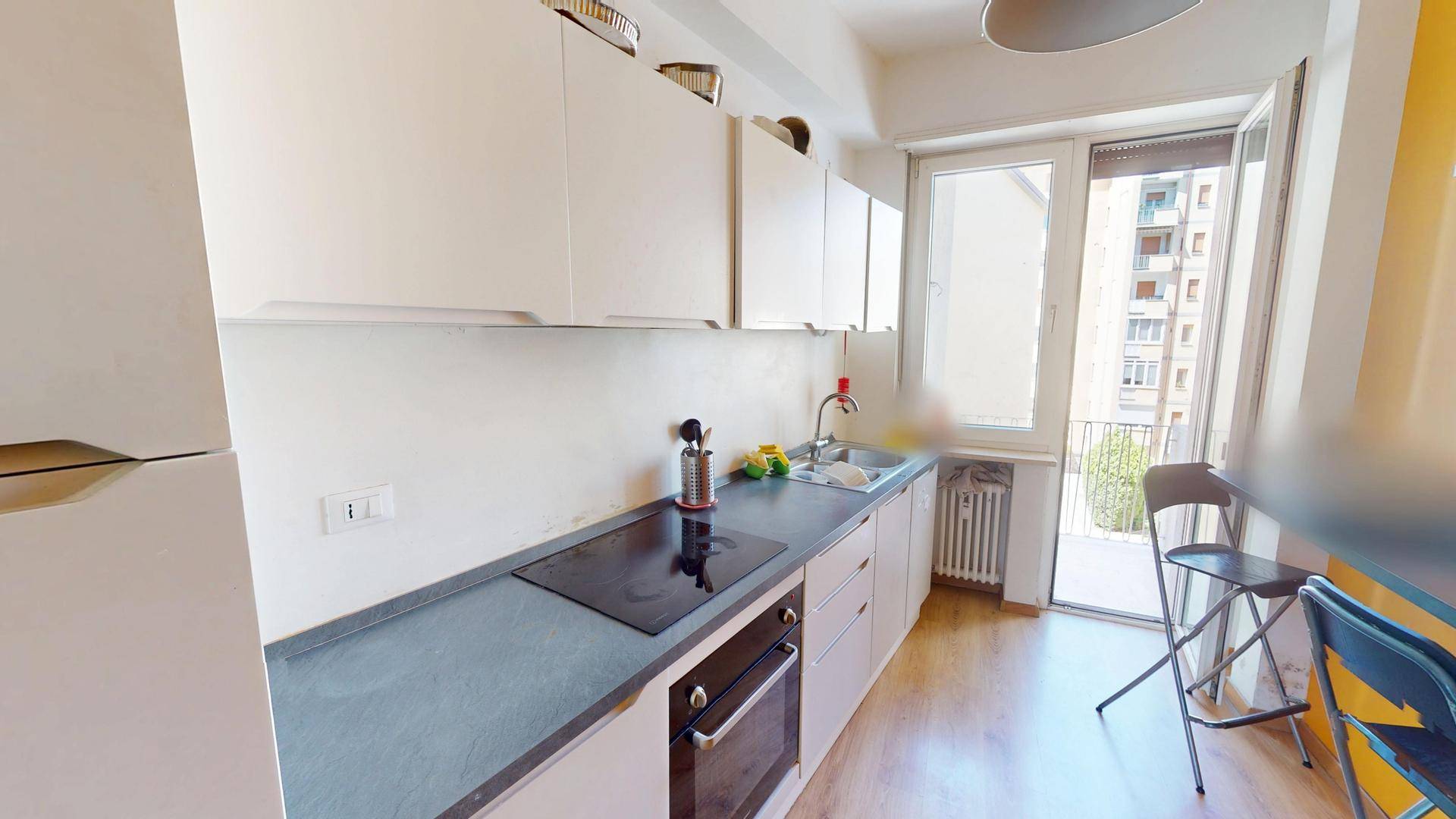Funktionale Küche mit weißen Schränken, Induktionskochfeld und Zugang zu einem kleinen Balkon.
