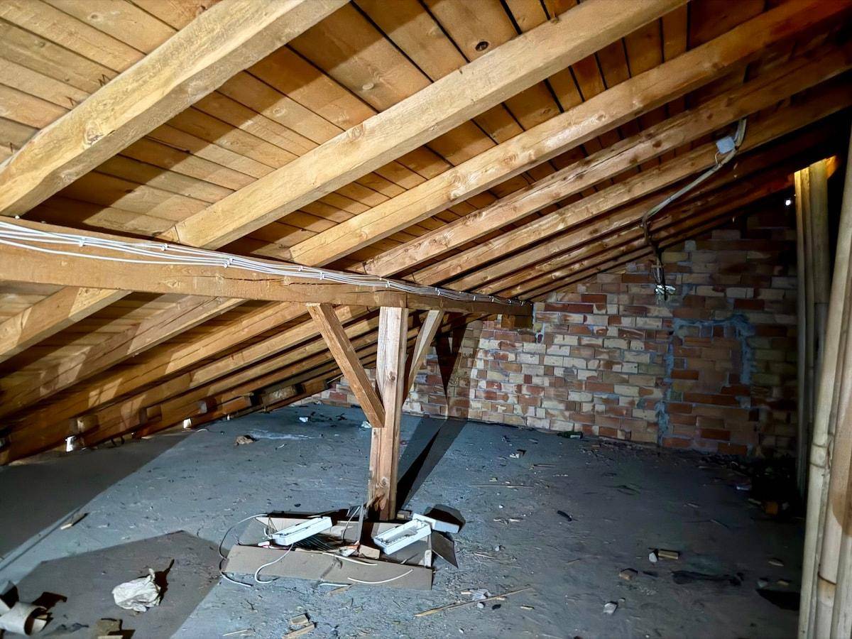 Unausgebauter Dachboden mit sichtbaren Holzbalken und Ziegelwänden, bietet Potenzial für Ausbau.