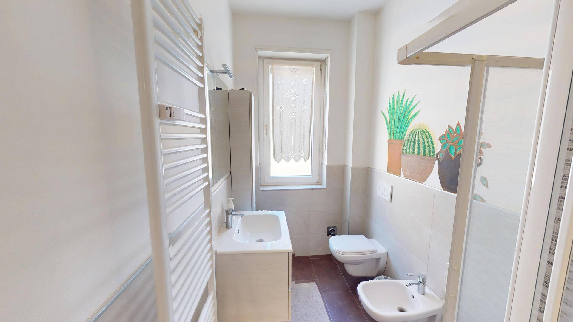 Helles Badezimmer mit Fenster, Dusche, Bidet und beheiztem Handtuchhalter.