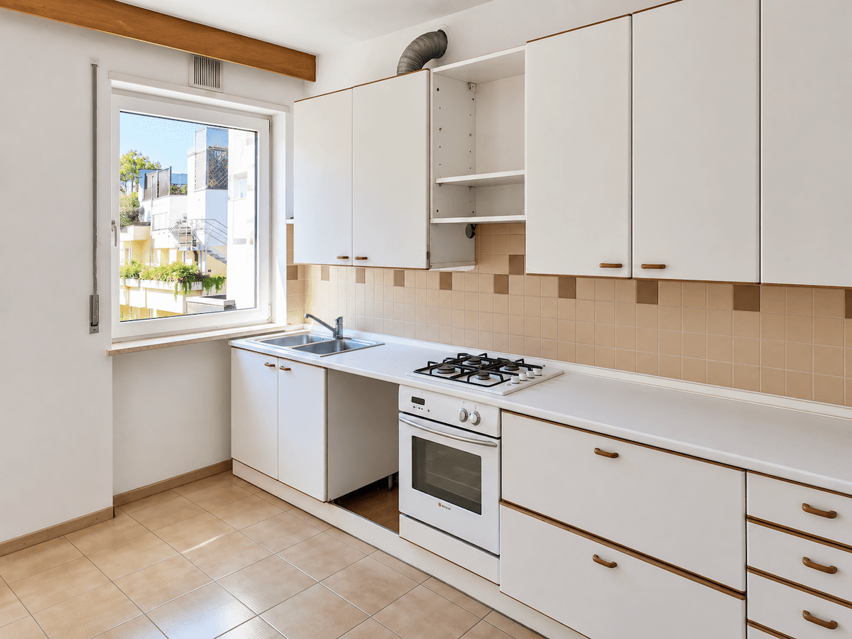 Leere Küche mit weißen Schränken, Gasherd, Backofen und Fenster mit Blick nach draußen.